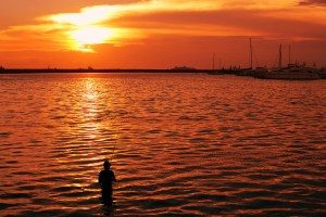 silhouette image of a fisherman in the water with golden reflection of a sunset.
